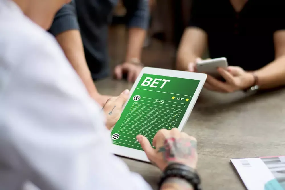 Dos personas frente a una tablet que muestra un campo de fútbol verde con la palabra «bet» en la pantalla.