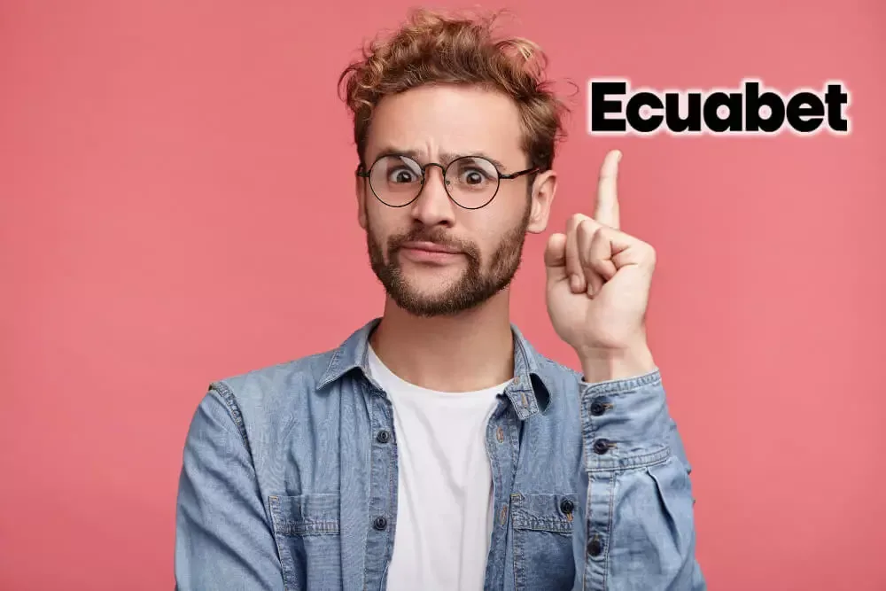 Hombre con gafas y camisa vaquera levantando el dedo índice sobre fondo rosa, junto al logotipo negro y amarillo de la marca.