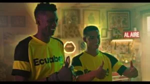 Dos personas con camiseta de Ecuabet frente a un cartel luminoso de «al aire», en una foto publicada por el sitio ecuabet.com.ec.