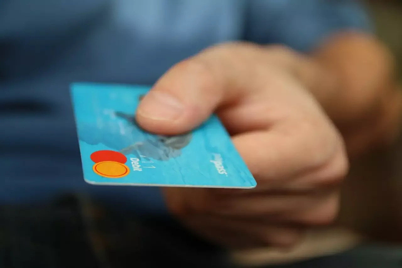 Primer plano de una mano sosteniendo una tarjeta bancaria azul frente a un fondo desenfocado.